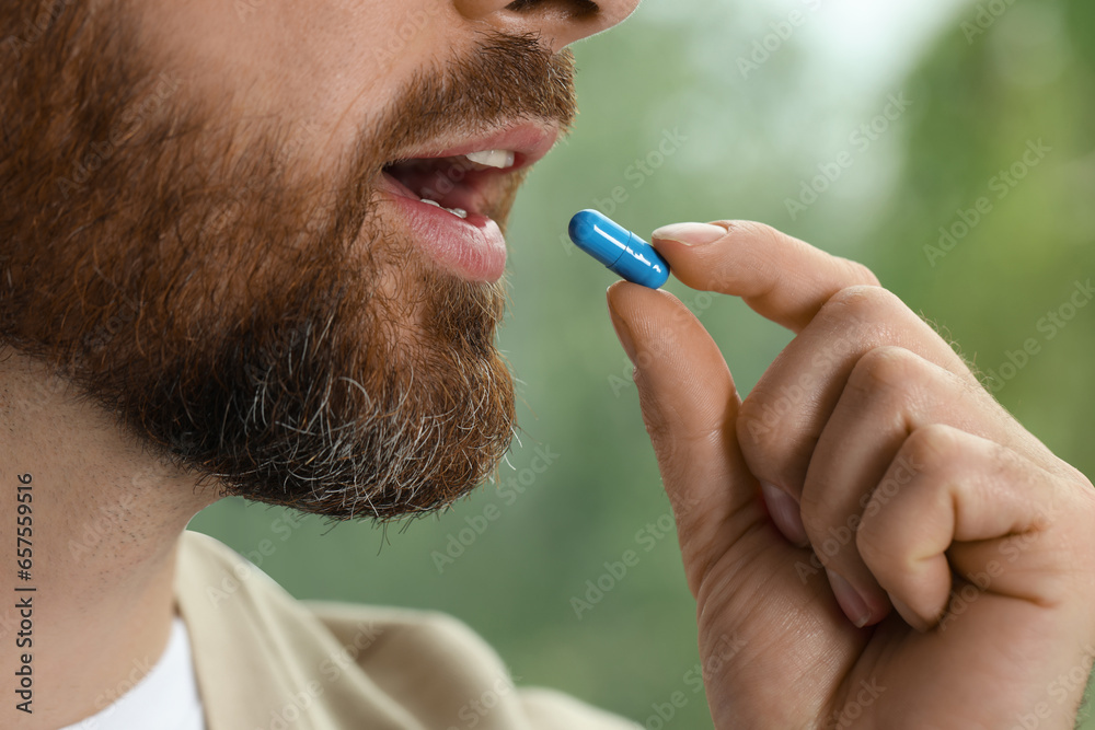 Poster Closeup view of bearded man taking pill on blurred background