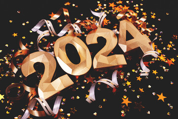 Closeup of golden 2024 numbers, glowing stars confetti and ribbons on a black background. New Year...