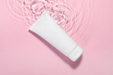 Tube of facial cleanser in water against pink background, top view