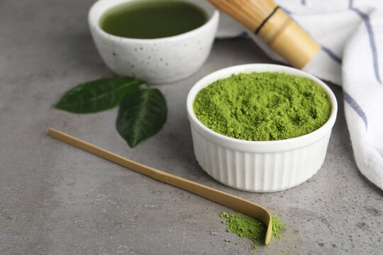 Green matcha powder and bamboo scoop on light grey table, closeup