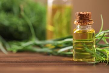 Bottle of essential oil and fresh tarragon leaves on wooden table. Space for text
