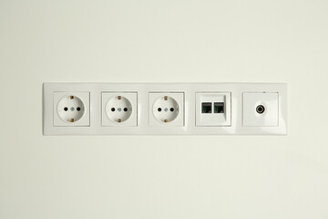 Many power sockets with ethernet and TV coax plates on white wall indoors