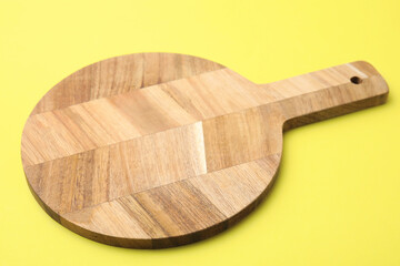 One wooden cutting board on yellow background, closeup. Cooking utensil