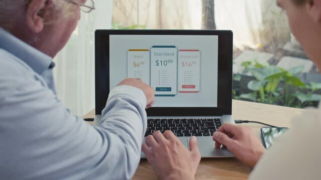 Back view of young and mature men choosing best option of online subscription for laptop, sitting at desk
