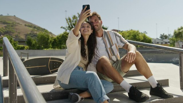 Happy young multiracial couple in casual clothing taking selfie with mobile phone at the skatepark