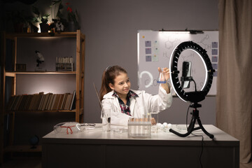 Chemistry research. Schoolgirl holding chemical flask in hands and showing it on camera recording...