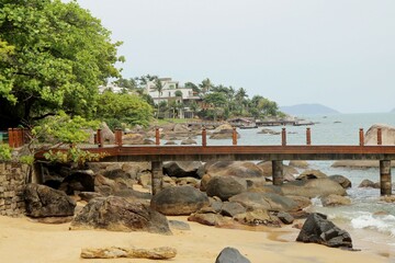 Pier on the beach crossing over stones, tropical palm trees and sea on background. Praia Grande, Ilha Bela, Brazil