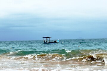 Small boat alone on blue sea, waves crashing beach and cloudy sky