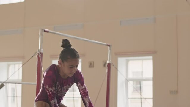 Elementary age Biracial girl in purple leotard performing elegant beam routine, doing handstand split and other artistic gymnastics elements on thin balance beam in choreography studio