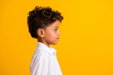 Side profile photo of funny schoolboy with curly hairdo dressed white shirt look at offer empty space isolated on yellow color background