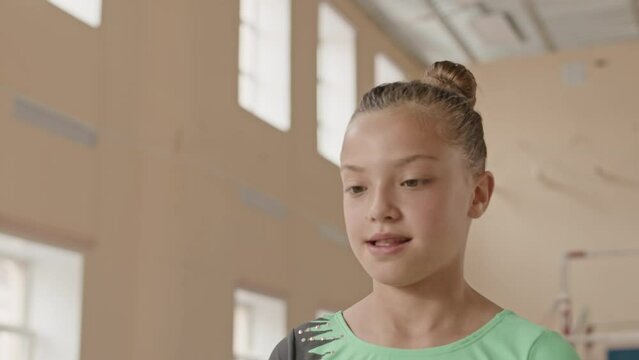 Slowmo of little acrobatic girl in green leotard performing split flip on floor in spacious gymnastics studio