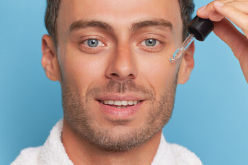 Handsome man doing cosmetic procedures, moisturizing skin with serum dropping tube, male beauty...