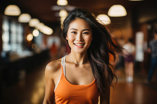 Portrait of a young Asian girl smiling, wearing a short orange dress, with long hair and an athletic complexion.
