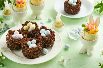 Easter chocolate nest cake with mini chocolate candy eggs with blossoming cherry or apple flowers on green background table. Creative recipe for Easter table with holiday decorations. Top view.