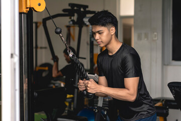 Fototapeta na wymiar A young handsome asian man does a set of tricep pushdowns at a hardcore gym.