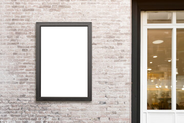 Vertical billboard mounted on a brick wall beside a shop door, offering an isolated surface ideal...