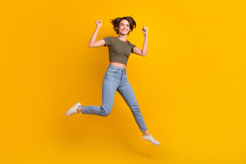 Fototapeta na wymiar Full length photo of lucky pretty lady wear khaki t-shirt rising fists jumping high isolated yellow color background