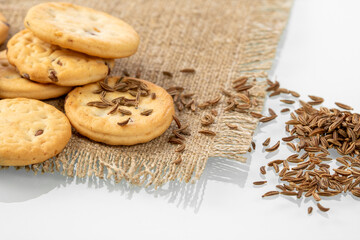 A pile of cumin cookies and scattered cumin seeds on a burlap napkin