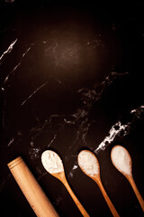 rolling pin and three wooden spoons with sugar salt and flour on a black marble background