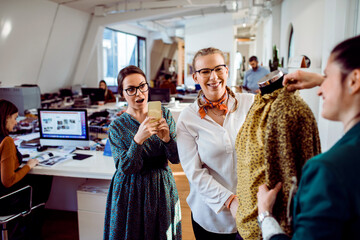 Group of female designers taking a picture on a smartphone of the finished product in a design firm