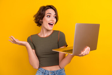 Photo of positive friendly girl with bob hairstyle dressed khaki t-shirt hold laptop talking on webcam isolated on yellow color background