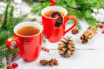 Hot winter or Christmas tea in ceramic red cups. Fir tree branches, lemon slice, spices and berries