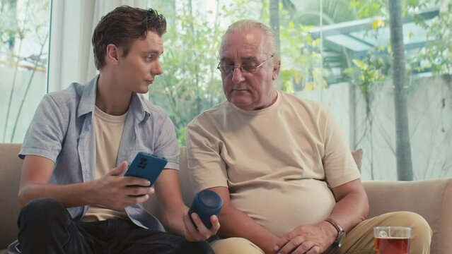 Medium shot of son showing father how to use smart speaker and connect to smartphone