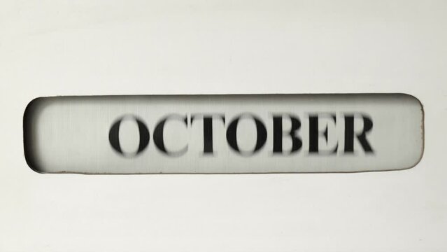 A retro office calendar is seen scrolling backwards through the months from December to January., to indicate moving to a New Year.  The text for the month is bold in black.