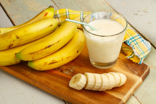 Vaso de leche natural y fresca junto a unos pl&aacute;tanos sobre un fondo de madera. Vista superior y de cerca. 