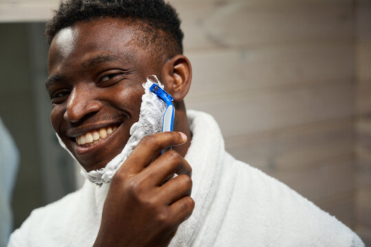 Smiling African American male shaves with a disposable razor