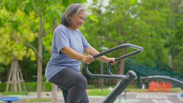 Senior Asian woman in casual workout in exercise stations in public park. Represents keeping young with physical activity, Open air gym. Physical health concept. Outdoor fitness equipment in city park
