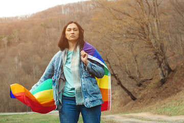 Woman holding the rainbow flag on the nature. Happiness, freedom and love concept for same sex couples.