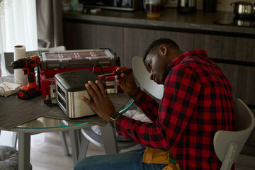 Young repairman is repairing a toaster on the kitchen table