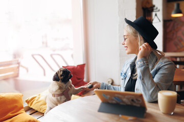 Lifestyle woman working on web tablet with pug dog at pets friendly cafe. Outdoor lifestyle work with Pet from anywhere concept