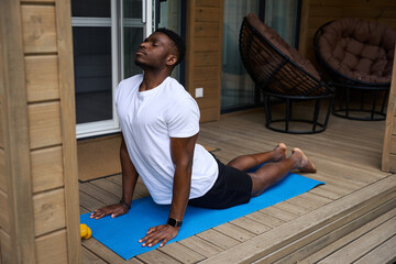 Naklejka premium Man practices yoga on a wooden terrace
