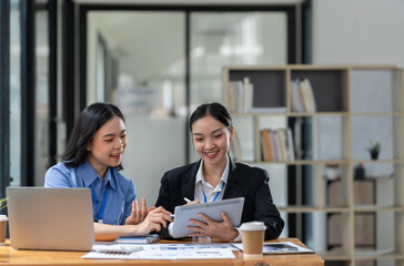 Two Asian businesswomen discuss investment project work and planning strategy Brainstorm together Find information online on iPad Laptop and tablet for making reports and summarizing business results
