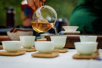 A woman pouring tea in a Chinese tea cup from a glass teapot