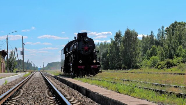 Steam locomotive drives on the railway passing the camera. Retro steam train departs from the railway station on bright sunny day. Vintage train