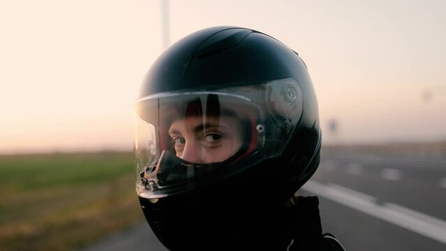 female motorcyclist in a helmet close-up at sunset.
