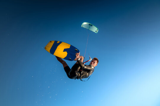 professional kiter performs a difficult trick against a beautiful blue sky background. Kitesurfing, Caucasian young man jump among clear sky
