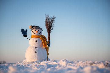 Snowman with broom on snowy field. Clear blue sky on background