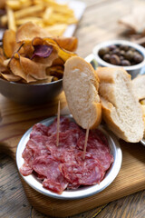 Appetizers or traditional tapas on a wooden table with cheese, olives, sausage, snacks and pieces of bread.