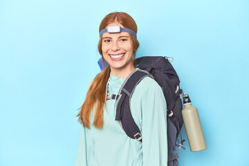 Redhead with backpack wearing headlamp on blue studio backdrop