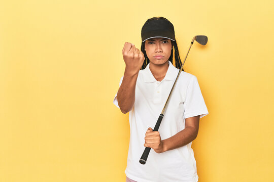 Indonesian female golfer on yellow backdrop showing fist to camera, aggressive facial expression.