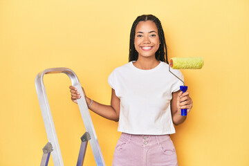 Indonesian woman with ladder and paint roller on yellow backdrop