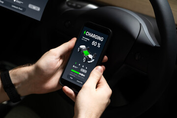 Electric car driver checks battery charging status, range and charging limit on app screen in the car. Smart technology device show EV car recharging data of electric storage in car battery innards.