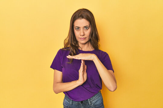 Middle-aged caucasian woman on yellow showing a timeout gesture.