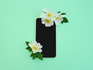 Creative layout made pink phone with black screen and white roses against pastel mint background. Girl essentials. Floral arrangement. Technology design.