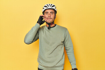 Casual dressed Latino cyclist on yellow with fingers on lips keeping a secret.