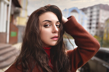 Beautiful girl in a brown coat on the street straightens her hair